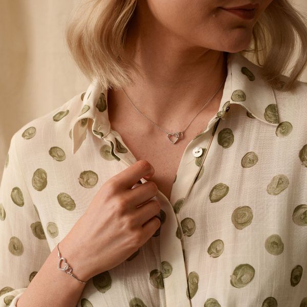 lady wearing a cream top with green flowers and blonde hair wearing a matching bracelet and necklace that have love hearts. 