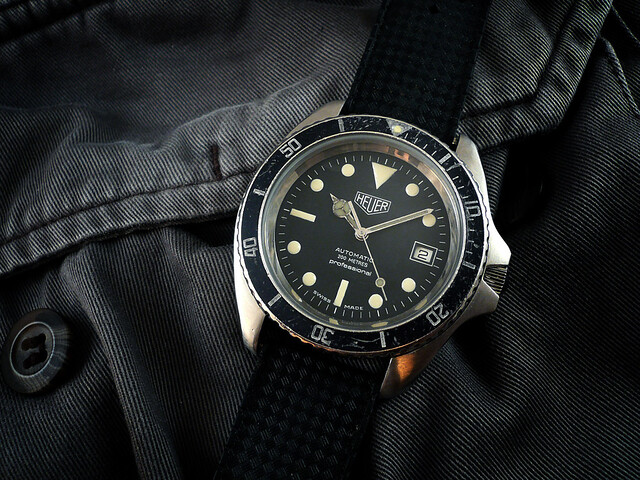 Heuer Reference Monnin 844 original watch from 1978 sat on denim jacket. Watch has a black dial and bezel and black strap