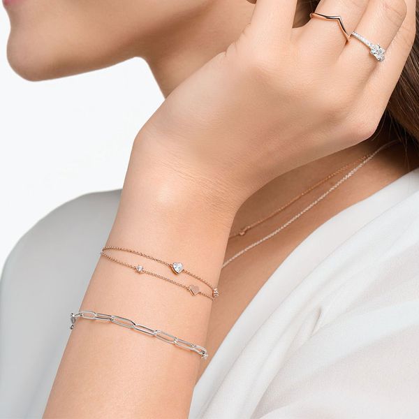 Lady wearing a white blouse with a number of pieces of jewellery. This features a silver paper-link bracelet and a rose gold double row bracelet on her wrist. With two rings, one rose gold and on silver. 