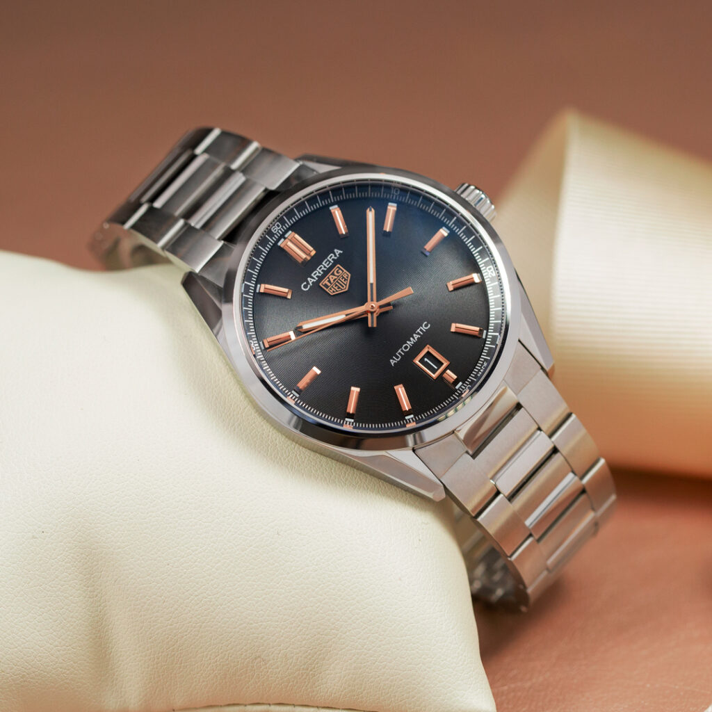 TAG Heuer Carrera steel watch with black and rose gold dial resting on a cream cushion