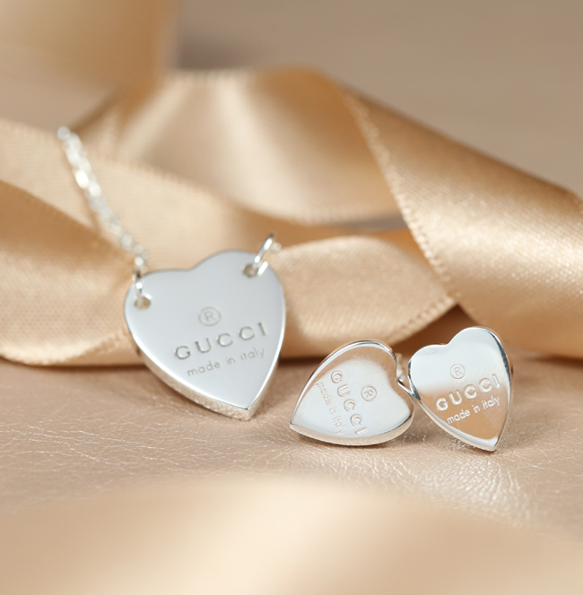Gucci silver love heart necklace on earring set resting against beige ribbon 